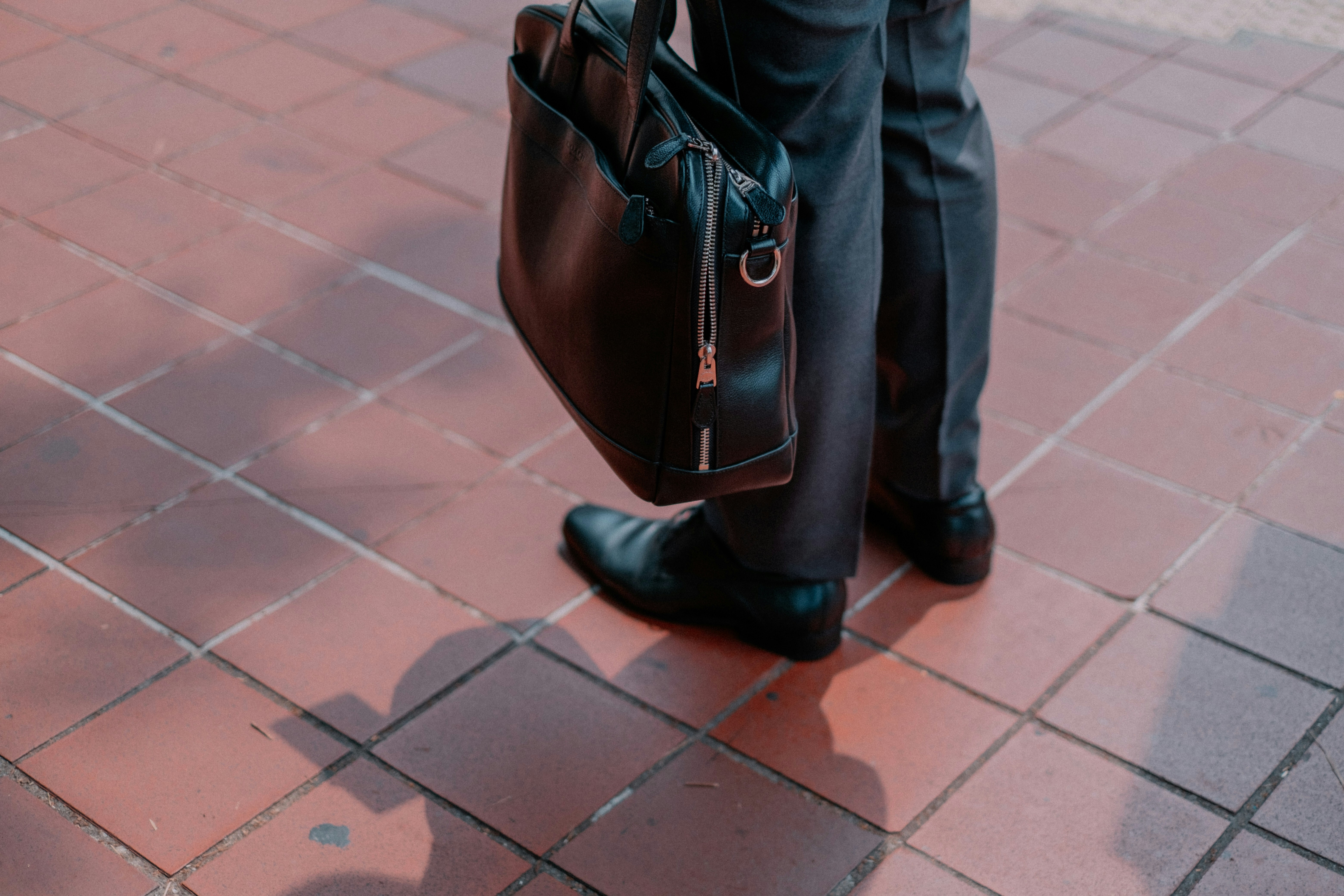 A businessman stands on terracotta tile with his briefcase visible