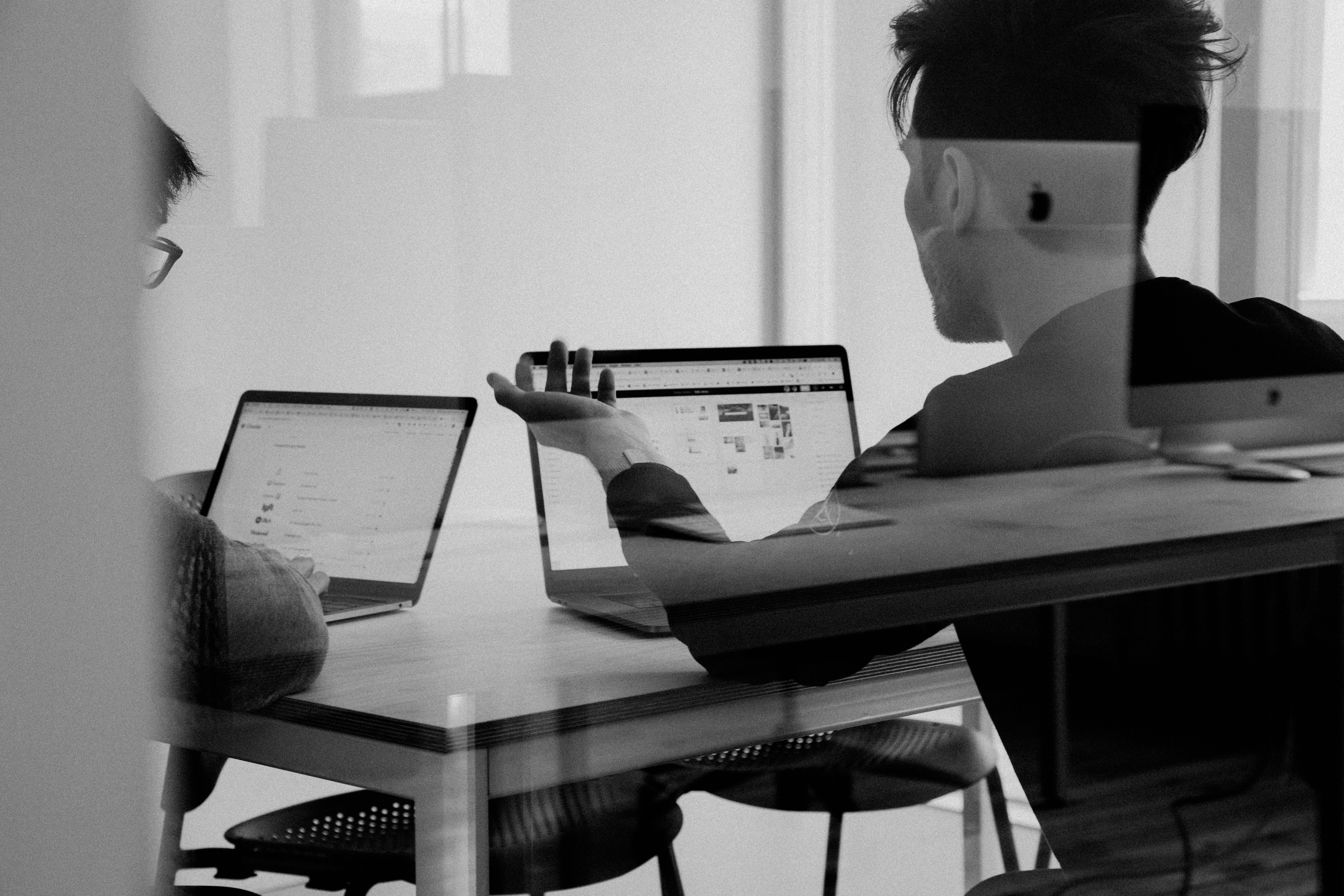 A black and white photo of two colleagues having a discussion with their laptops