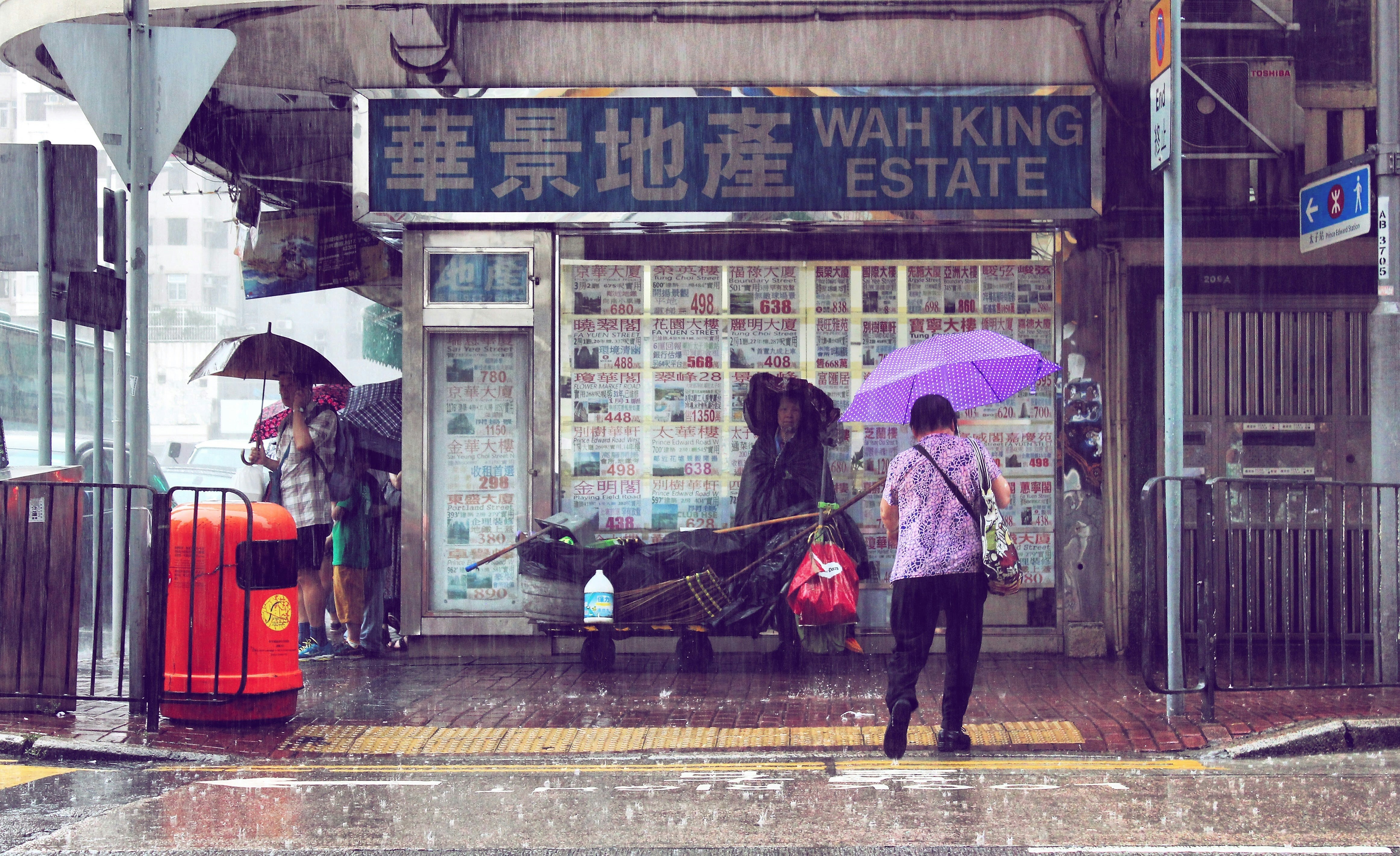 A woman with a purple umbrella stands in front of an estate agent in the rain