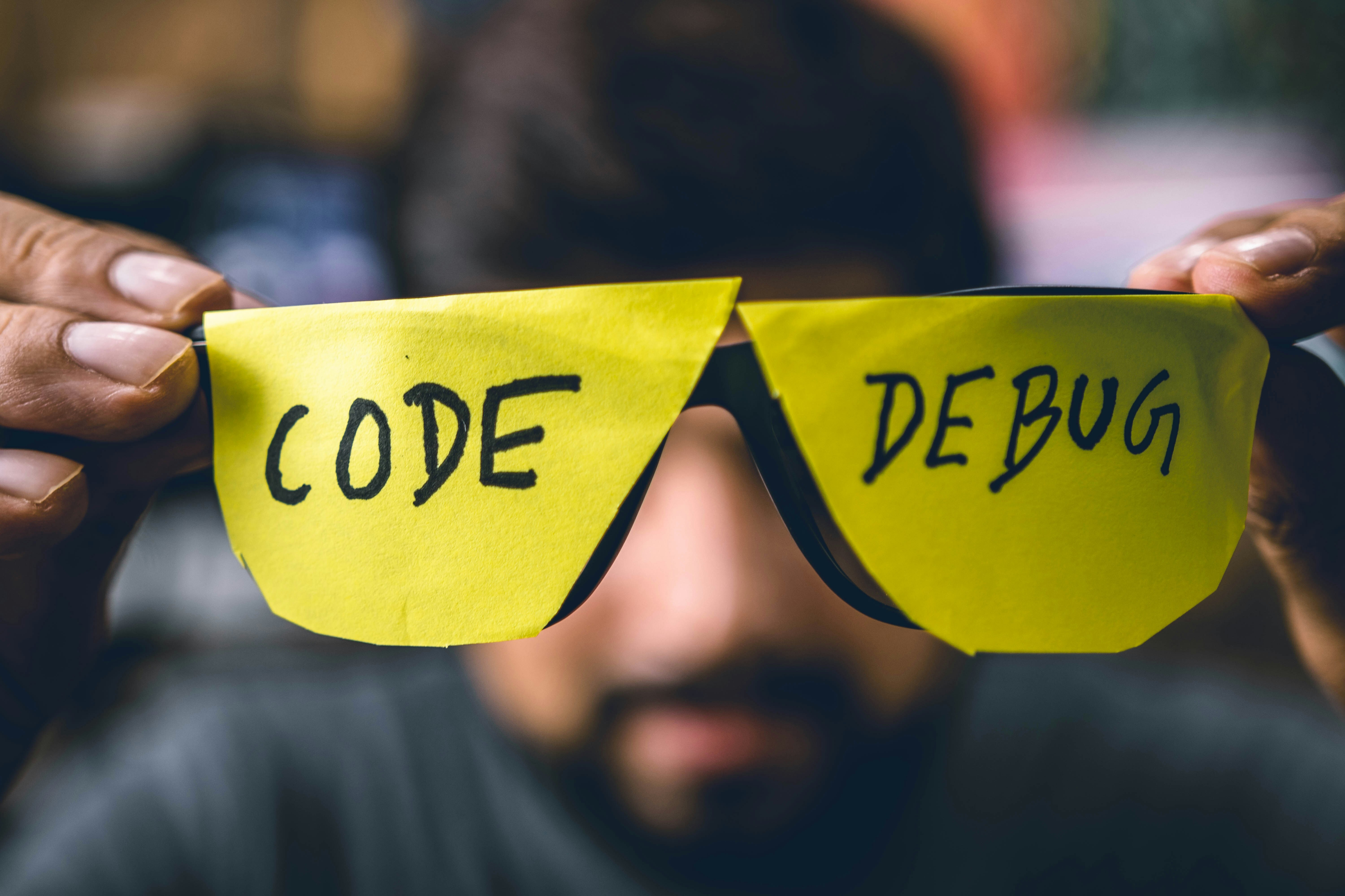 A man holding a pair of glasses that say "Code" "Debug" on either lens.