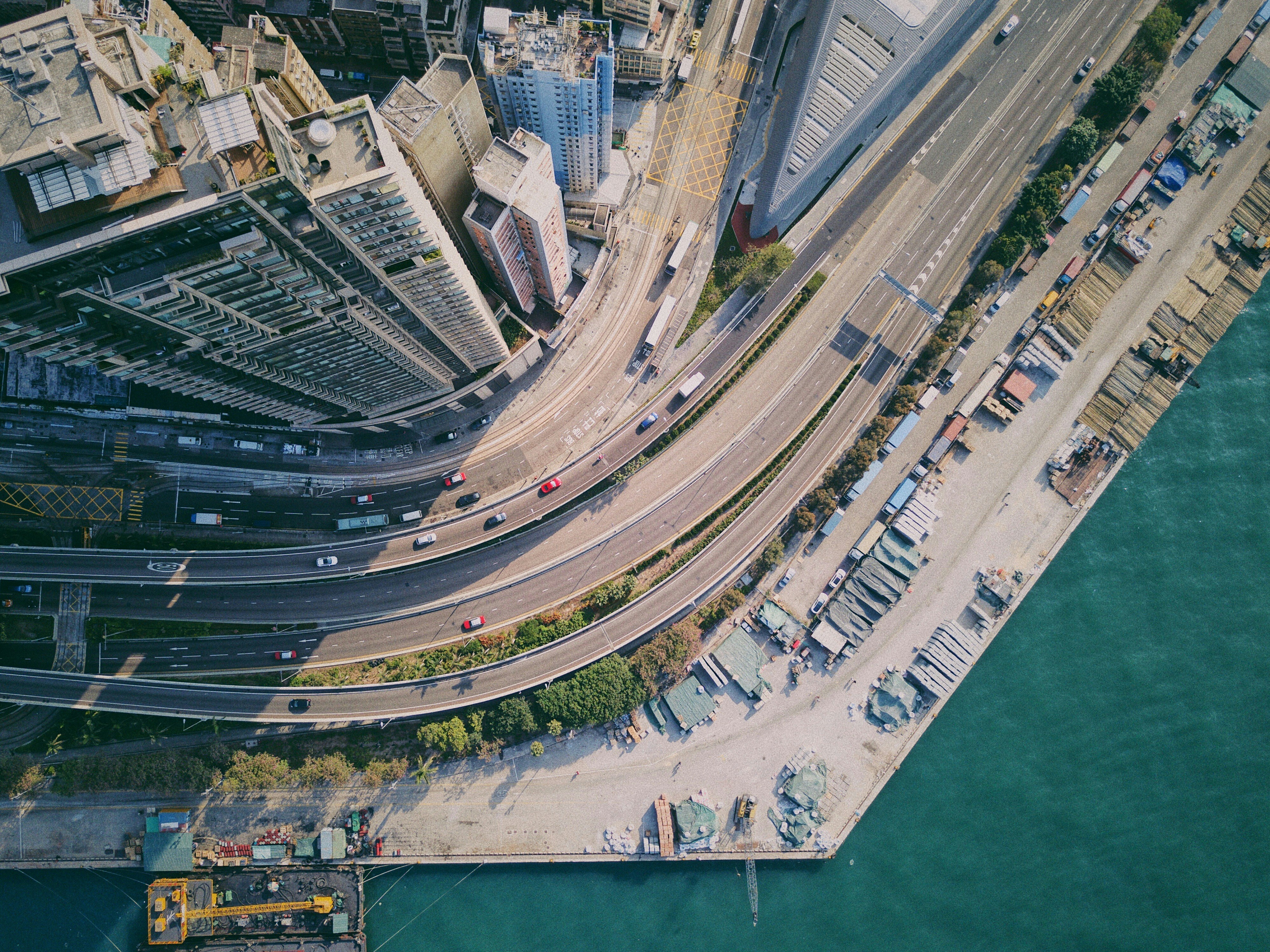 A top down view of a Hong Kong Highway. It is a sunny day. A skyscraper is casting a shadow.