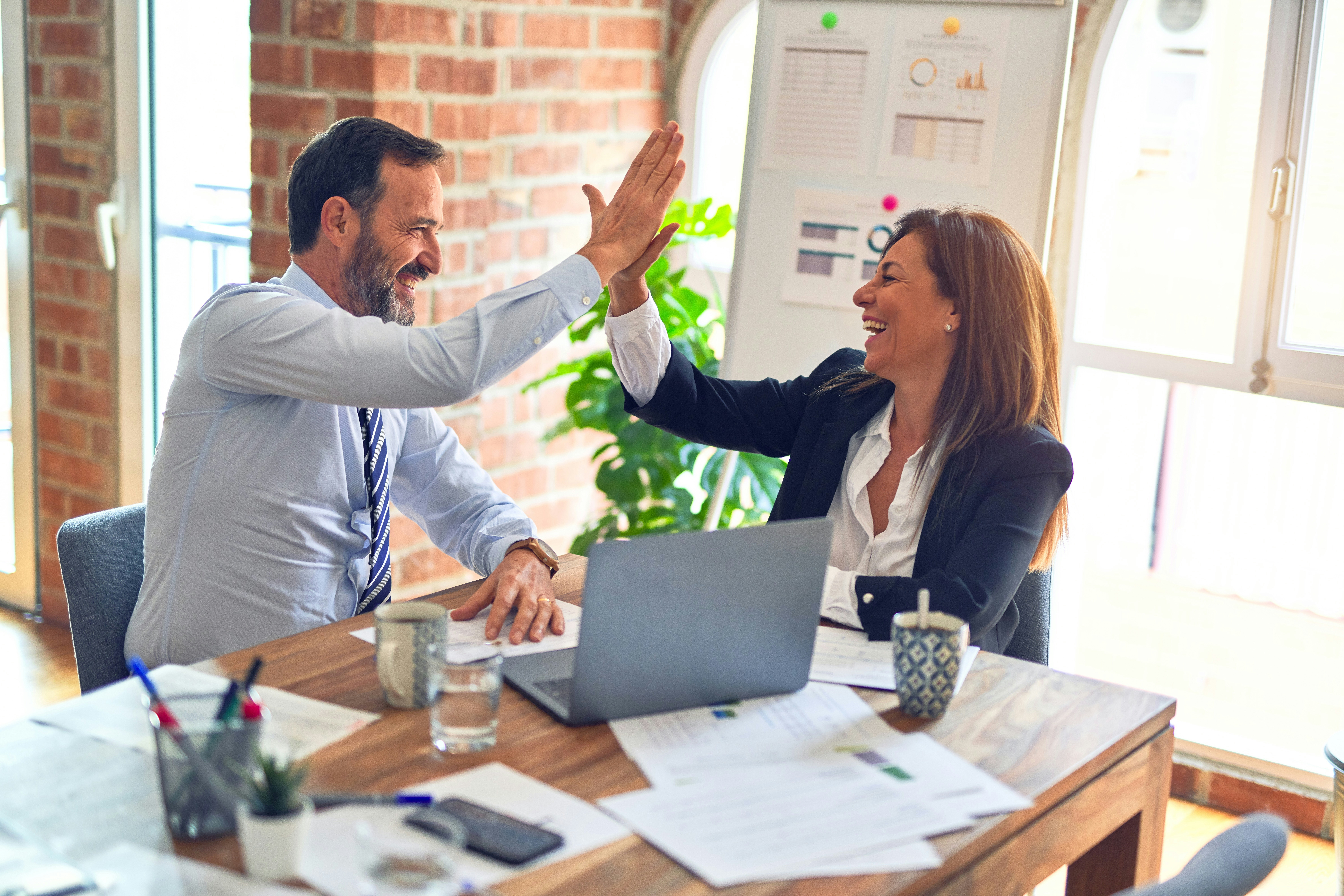 Two people sharing a high five over paperwork and a computer