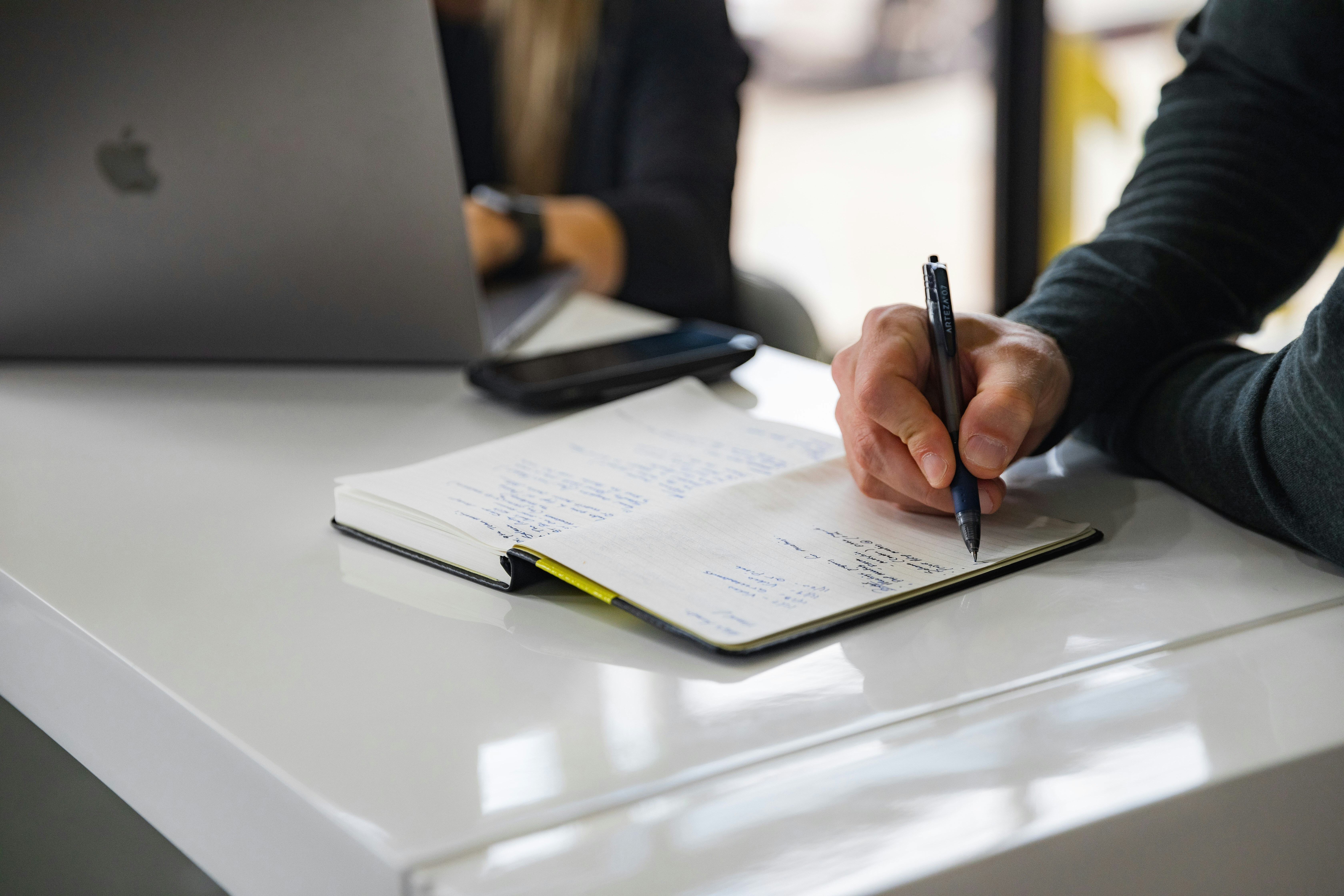 A person writing in a notebook at a business meeting