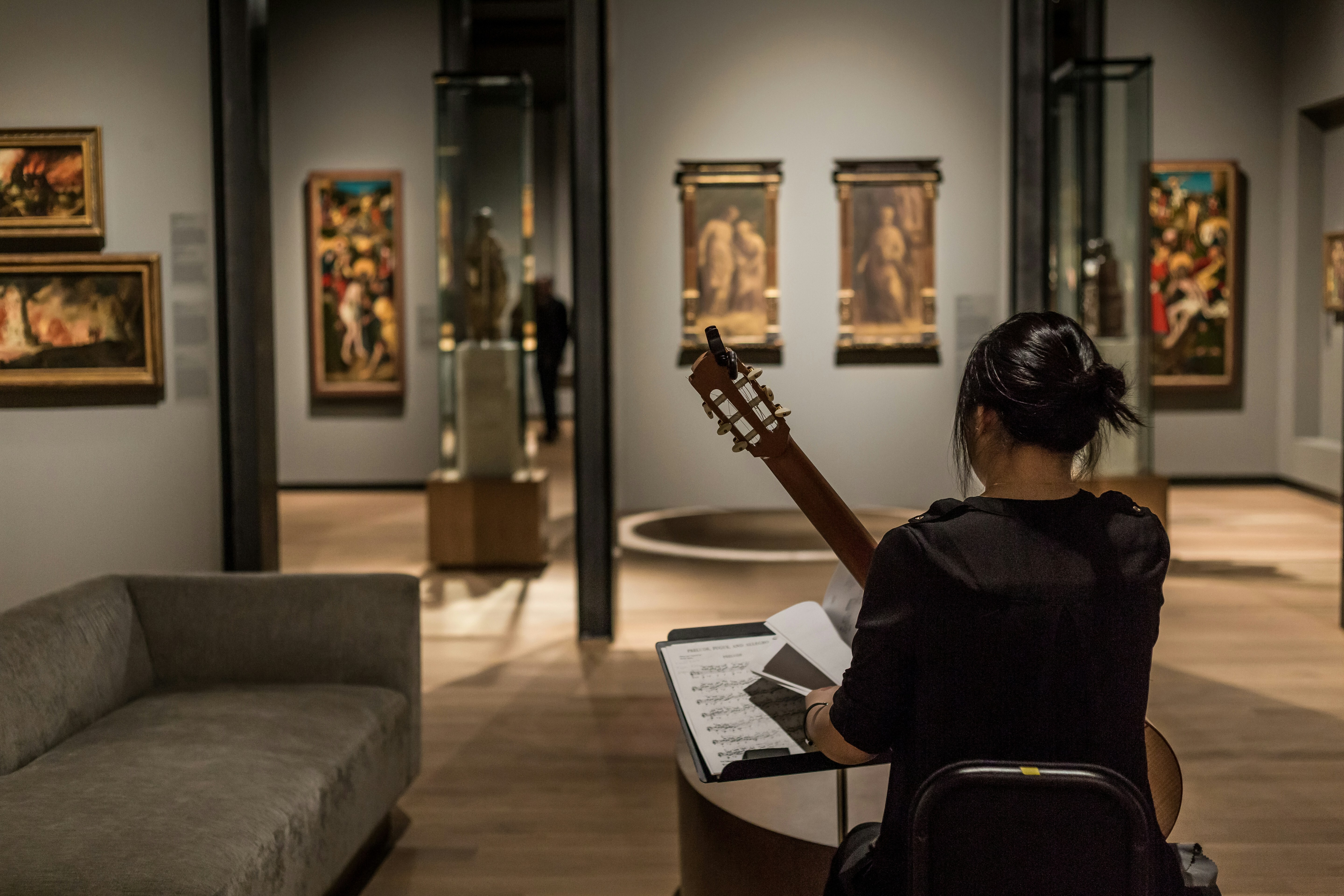 a guitar player in a gallery space surrounded by hanging art