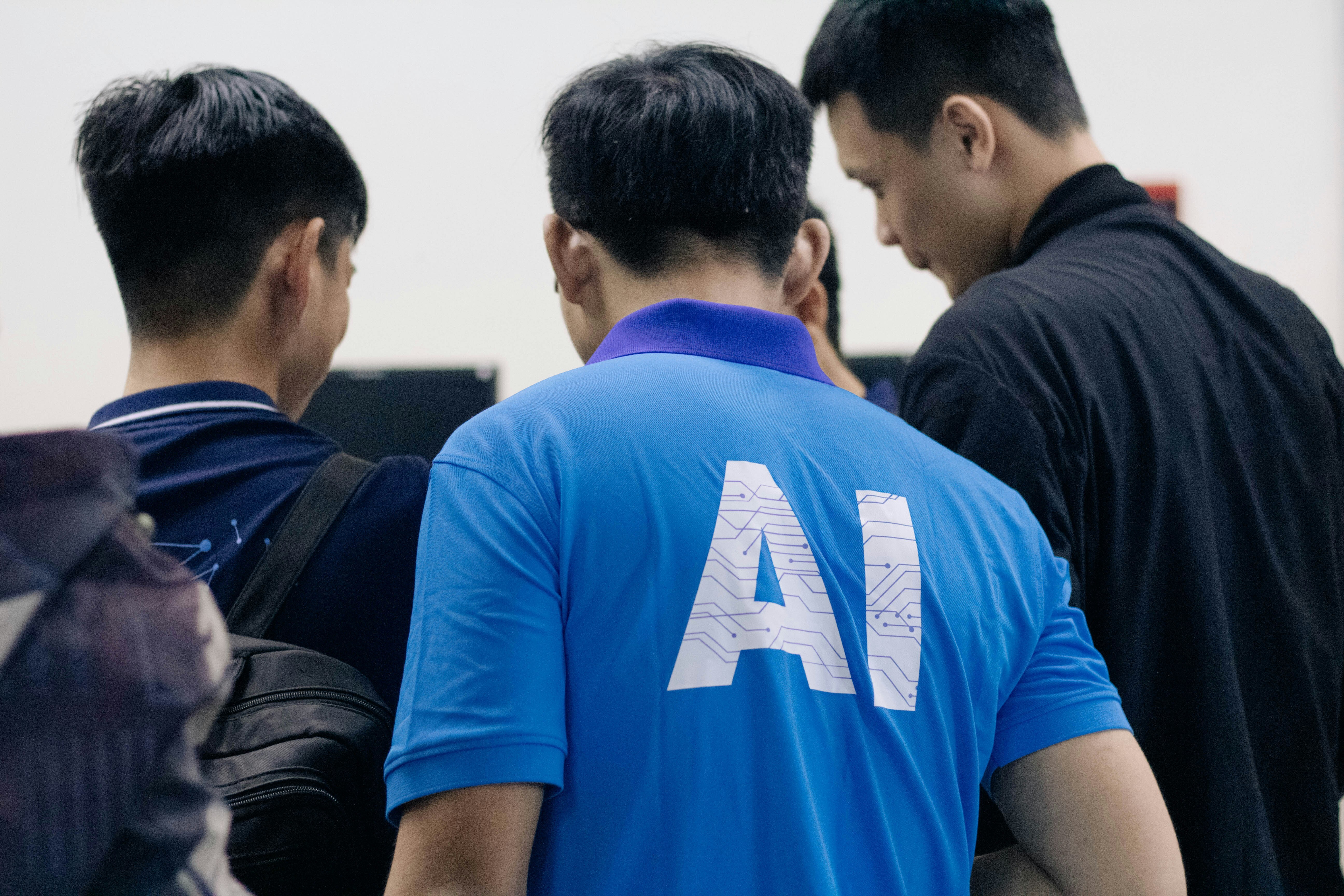 A man in a blue AI shirt talking to another group of men at a technical conference.