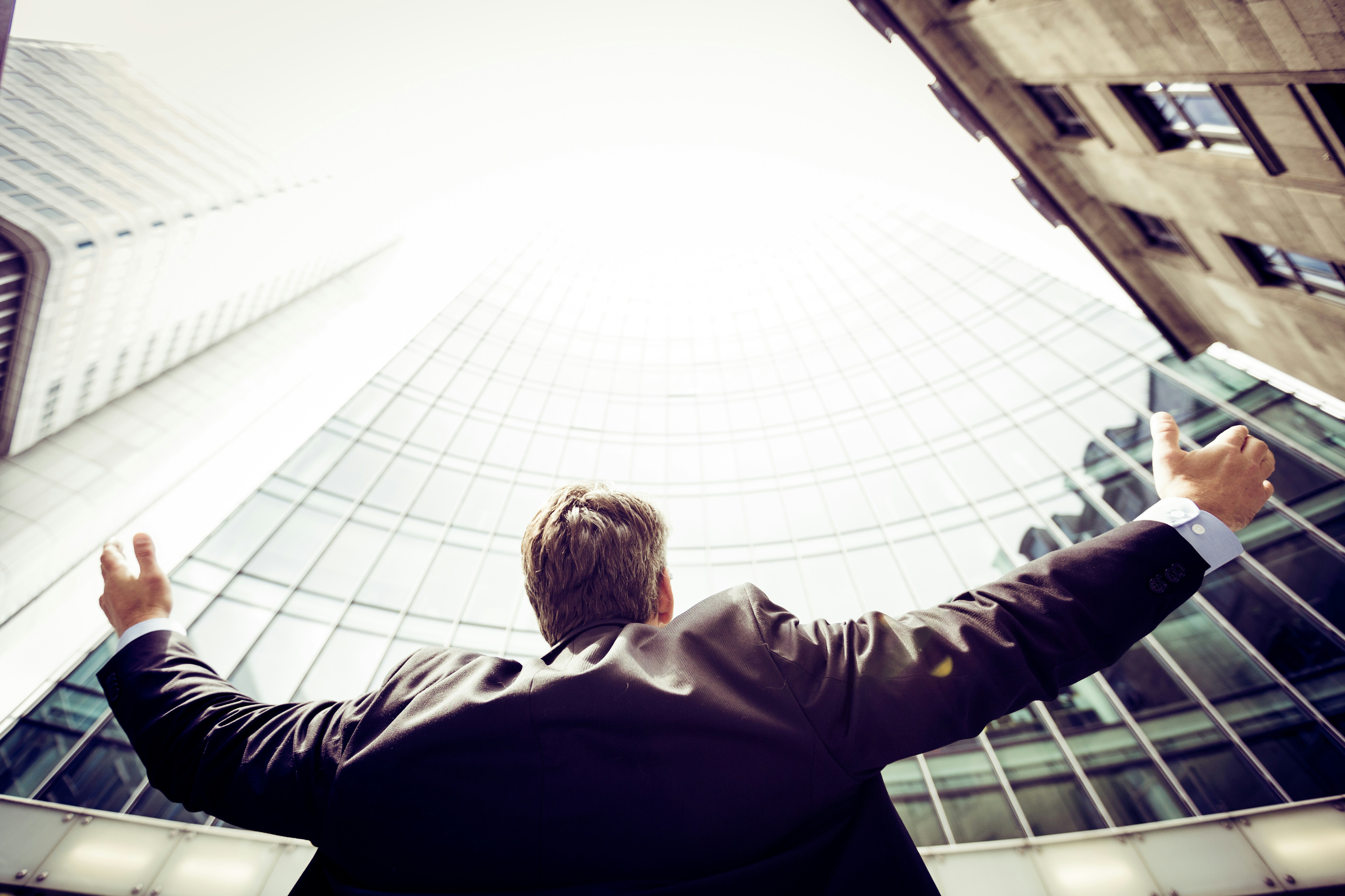 A businessman stands with arms outstretched in joy at the base of a modern office building