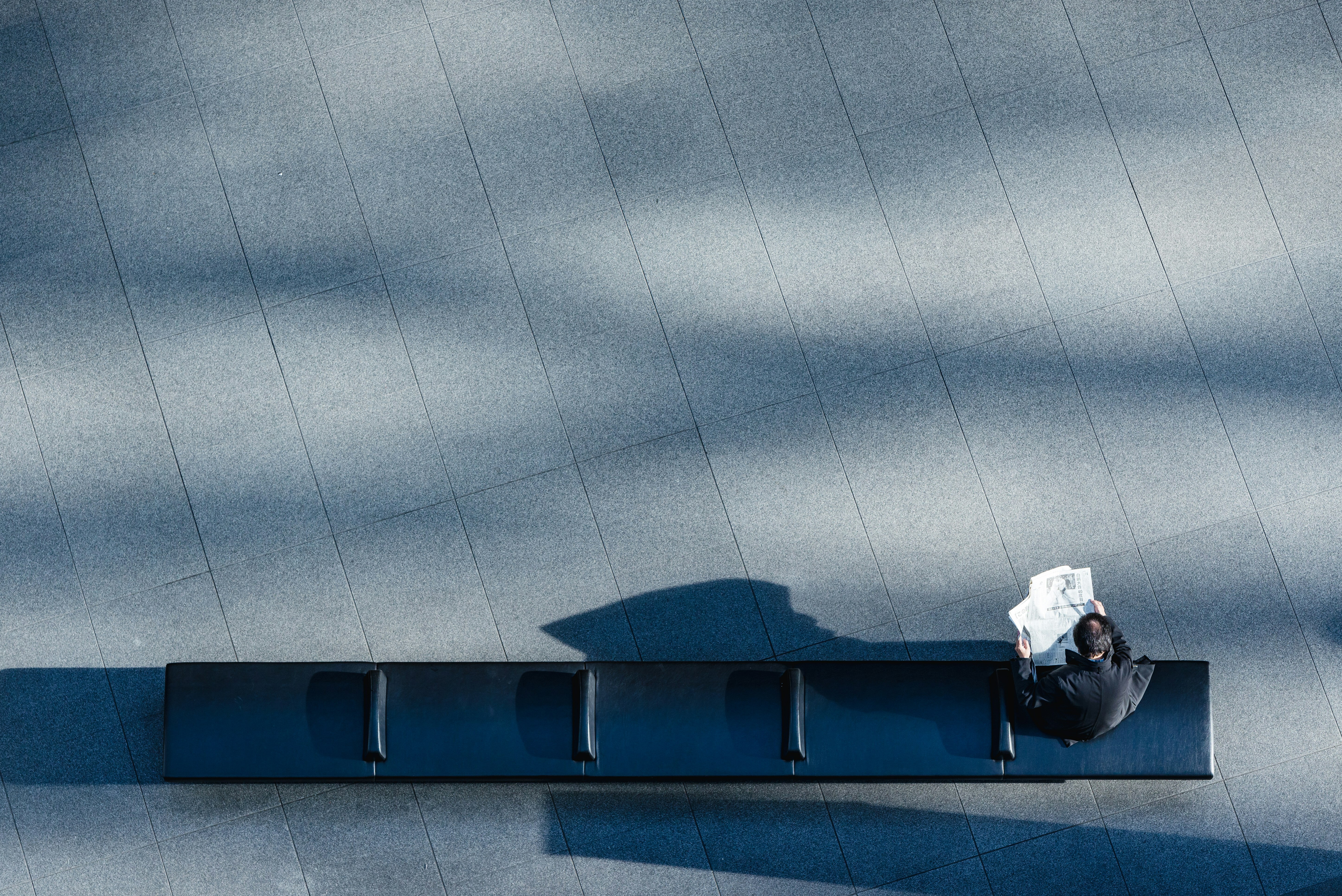 A top view of a lone businessman sitting on a bench reading a paper in an empty plaza